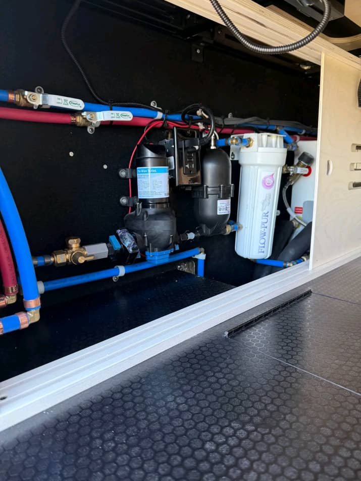 RV water system with FloWater filtration, plumbing lines, and pressure pump inside a 2024 Mercedes-Benz Sprinter 2500.